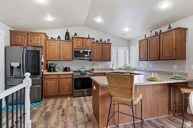 3295 S 1500 W, Perry, UT 84302 - kitchen featuring vaulted ceiling, light wood-style floors, a peninsula, a kitchen bar, and appliances with stainless steel finishes