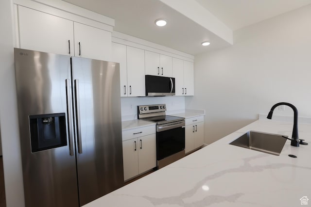 kitchen with white cabinets, recessed lighting, a sink, light stone countertops, and appliances with stainless steel finishes