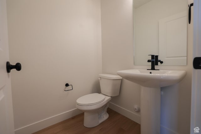 half bathroom featuring wood finished floors, toilet, and baseboards