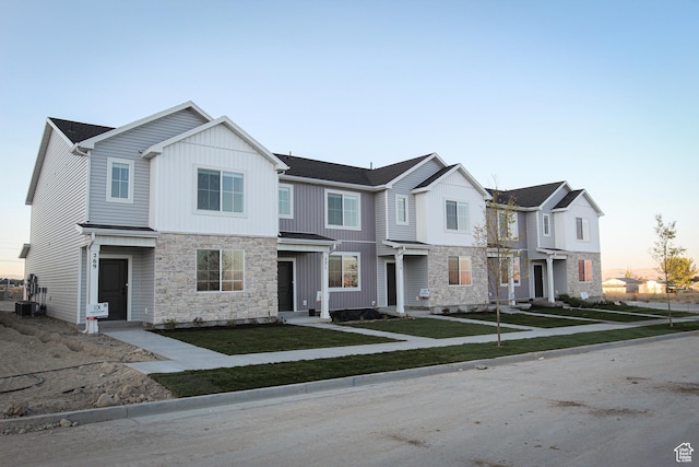 view of property with stone siding, a front lawn, board and batten siding, and cooling unit