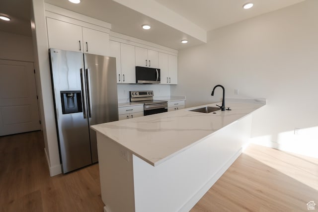 kitchen featuring wood finished floors, a sink, a peninsula, appliances with stainless steel finishes, and recessed lighting
