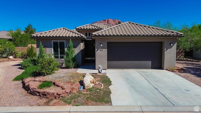 mediterranean / spanish house with an attached garage, concrete driveway, a tiled roof, and stucco siding