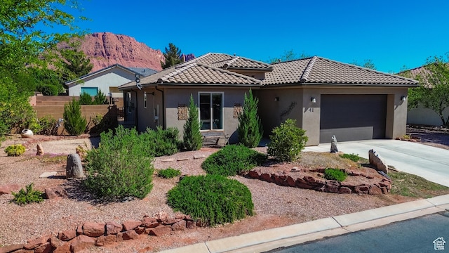 view of front of house with a tiled roof, concrete driveway, fence, a garage, and stucco siding