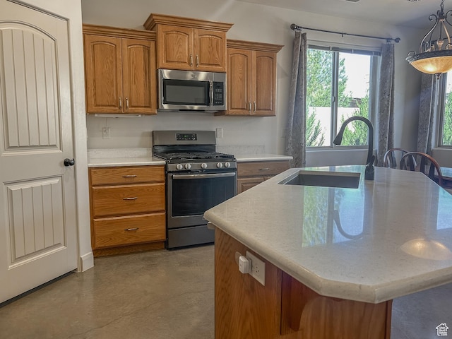 kitchen featuring an island with sink, a sink, concrete flooring, brown cabinetry, and appliances with stainless steel finishes