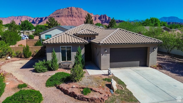 view of front facade featuring a tile roof, driveway, a mountain view, a garage, and stucco siding