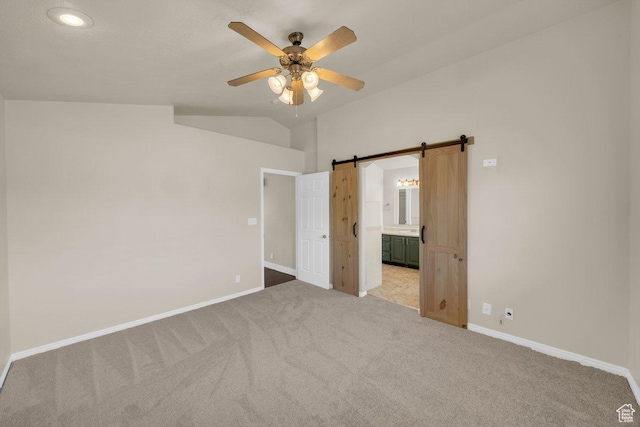 unfurnished bedroom with a barn door, ensuite bathroom, light colored carpet, baseboards, and lofted ceiling