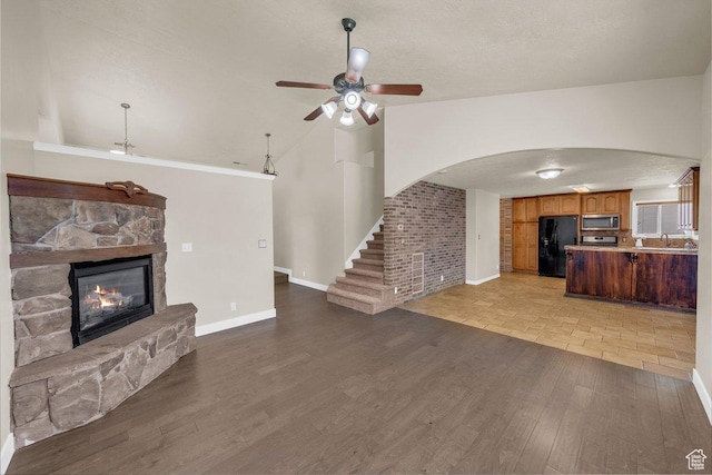 unfurnished living room with arched walkways, baseboards, wood finished floors, ceiling fan, and a stone fireplace