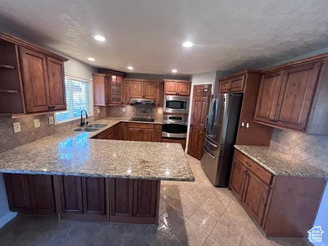 kitchen with a sink, stainless steel appliances, backsplash, a peninsula, and under cabinet range hood