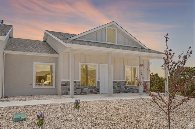1152 E Smokey Trail Way, Cedar City, UT 84721 - back of house at dusk with board and batten siding, a shingled roof, and stone siding