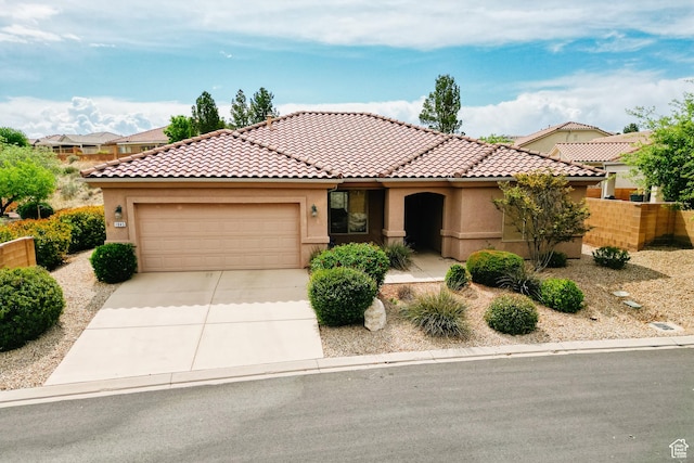 mediterranean / spanish-style home with an attached garage, a tiled roof, stucco siding, and driveway