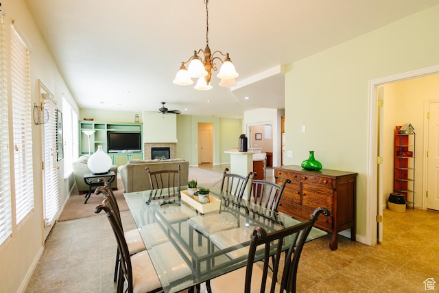 dining room featuring light floors, baseboards, a glass covered fireplace, and ceiling fan with notable chandelier
