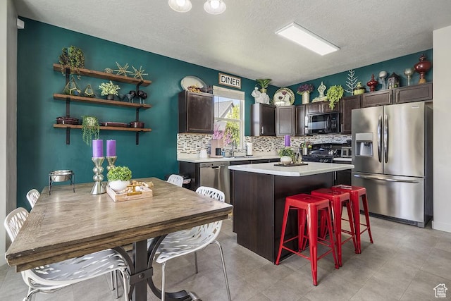 6961 W Goblin Valley Cv S, West Jordan, UT 84081 - kitchen featuring a textured ceiling, dark brown cabinetry, light countertops, appliances with stainless steel finishes, and a kitchen island