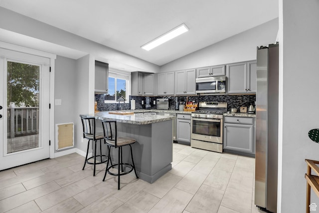 kitchen featuring gray cabinets, decorative backsplash, lofted ceiling, and stainless steel appliances