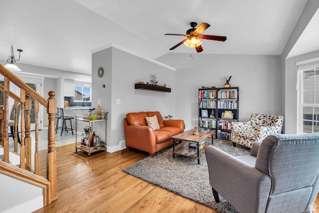 living area featuring stairway, a ceiling fan, light wood-style flooring, baseboards, and lofted ceiling