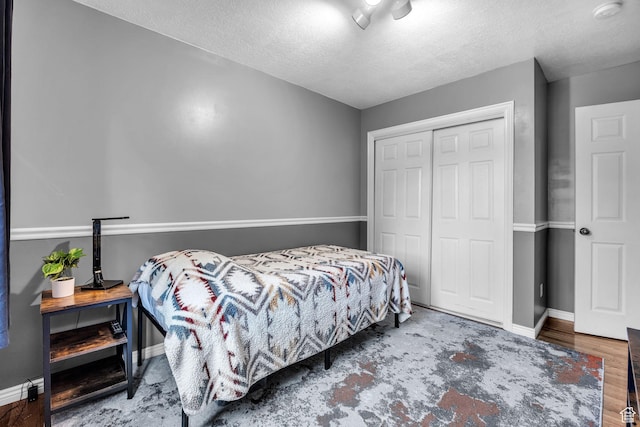 bedroom featuring baseboards, wood finished floors, a textured ceiling, and a closet