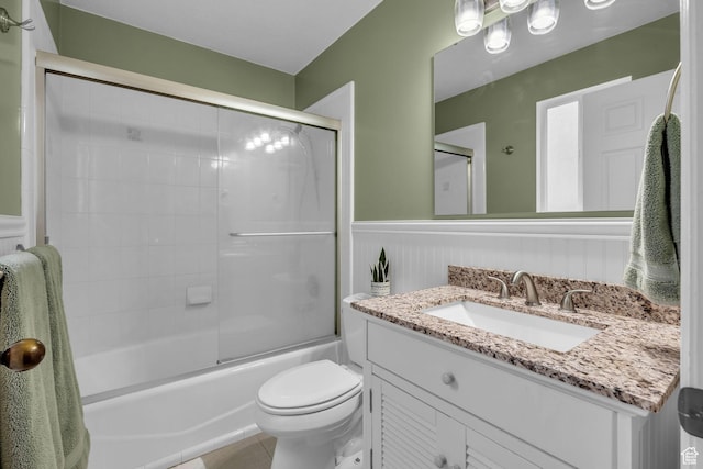 bathroom featuring tile patterned floors, a wainscoted wall, bath / shower combo with glass door, toilet, and vanity