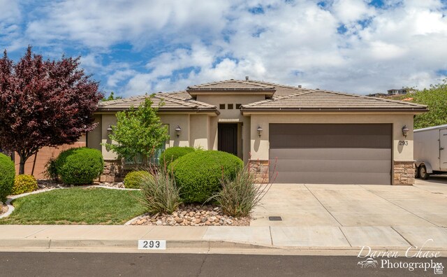 prairie-style home with stucco siding, concrete driveway, a tile roof, stone siding, and a garage