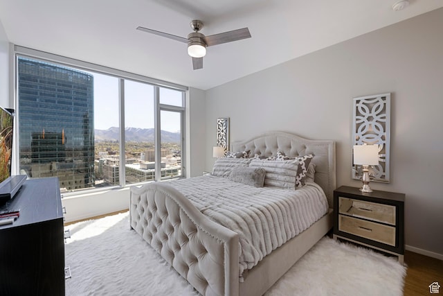 bedroom featuring light wood finished floors, baseboards, ceiling fan, and a mountain view