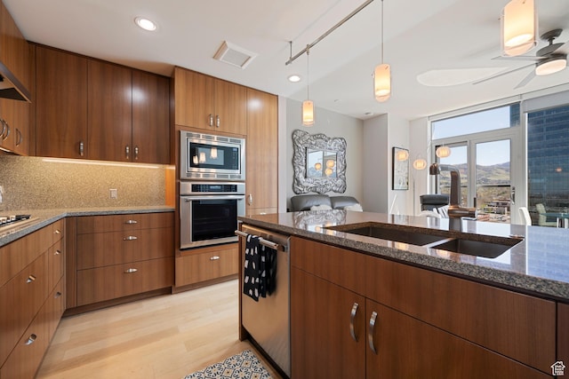 kitchen with dark stone counters, a sink, pendant lighting, light wood finished floors, and appliances with stainless steel finishes