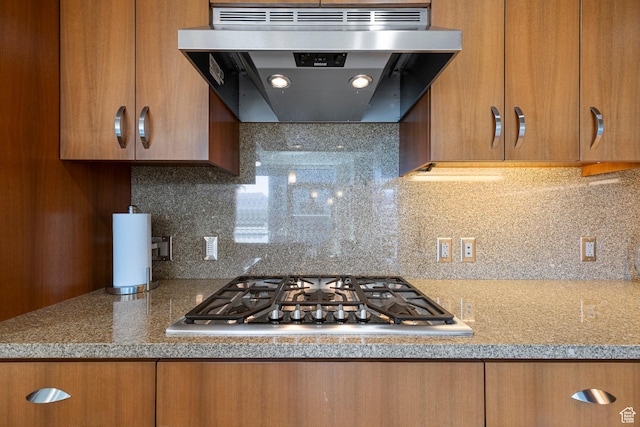 kitchen featuring stainless steel gas stovetop, under cabinet range hood, light countertops, brown cabinetry, and tasteful backsplash