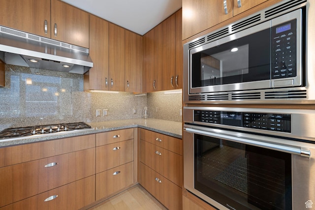 kitchen featuring stainless steel appliances, under cabinet range hood, decorative backsplash, and light stone counters