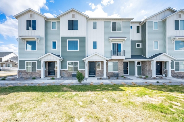multi unit property with board and batten siding, stone siding, a front yard, and central AC unit