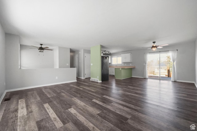 unfurnished living room with ceiling fan, visible vents, dark wood-style floors, and baseboards