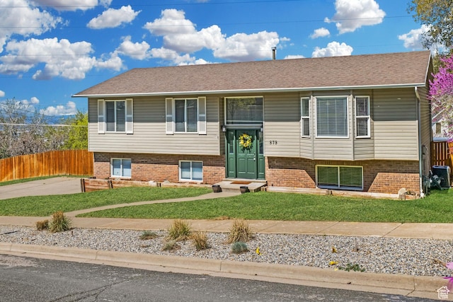 split foyer home with a front lawn, fence, central AC, and brick siding