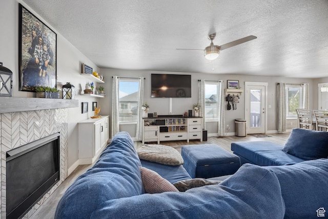 2448 W Anne Ave S, West Haven, UT 84401 - living room with a ceiling fan, a textured ceiling, light wood-style flooring, a fireplace, and baseboards