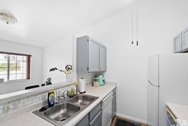 kitchen with a sink, white appliances, gray cabinets, light countertops, and backsplash