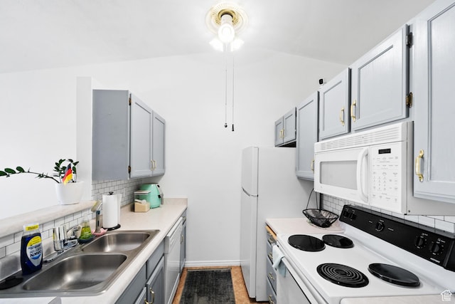 kitchen featuring a sink, white appliances, gray cabinets, light countertops, and backsplash
