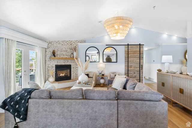 living room featuring a brick fireplace, a wainscoted wall, wood finished floors, lofted ceiling, and visible vents