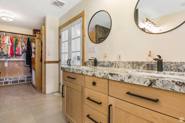 full bathroom with double vanity, a walk in closet, tile patterned floors, and visible vents