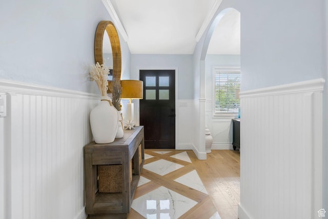 entryway featuring arched walkways, wainscoting, and light wood-style flooring