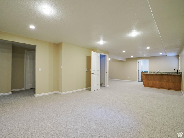 finished below grade area featuring recessed lighting, baseboards, a textured ceiling, light colored carpet, and indoor wet bar