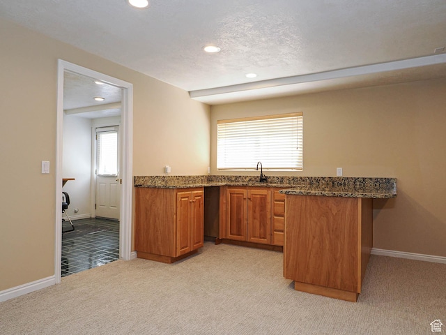 kitchen featuring dark stone counters, baseboards, recessed lighting, light colored carpet, and brown cabinetry