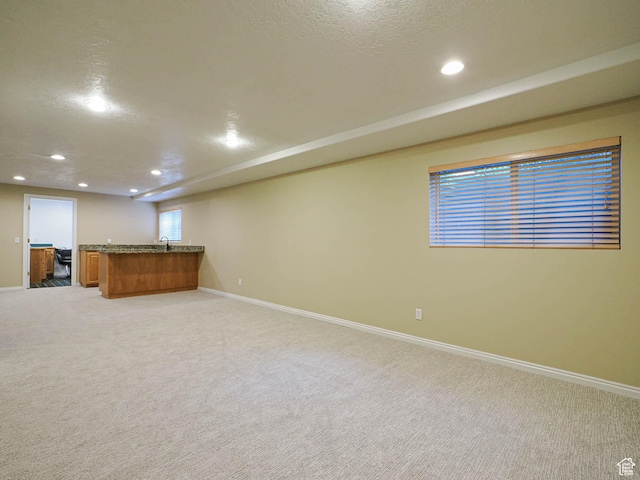 below grade area with light carpet, a textured ceiling, baseboards, recessed lighting, and indoor wet bar