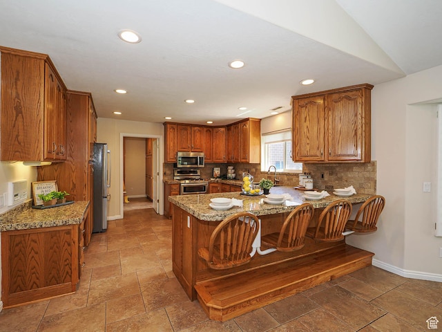 kitchen featuring baseboards, recessed lighting, backsplash, brown cabinetry, and appliances with stainless steel finishes
