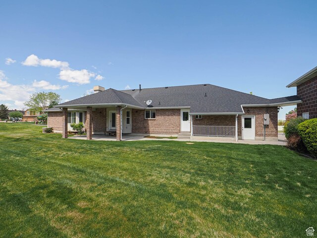 back of property featuring brick siding, a yard, a patio area, and a shingled roof