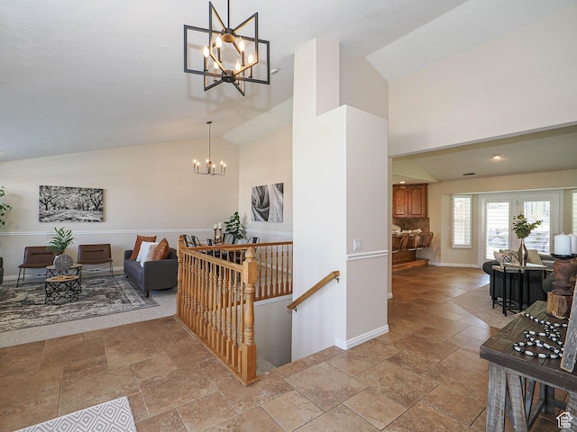 hallway featuring high vaulted ceiling, an upstairs landing, stone tile flooring, baseboards, and a notable chandelier