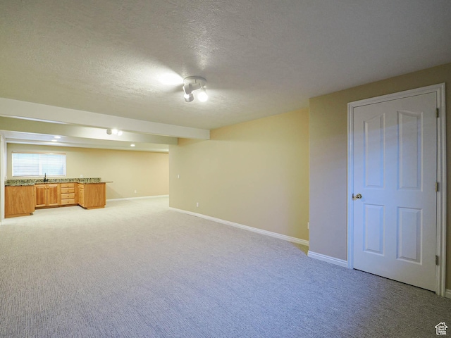 below grade area featuring light carpet, baseboards, a textured ceiling, and bar area