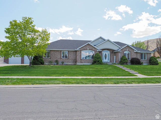 view of front facade with a front lawn, roof with shingles, driveway, brick siding, and a garage