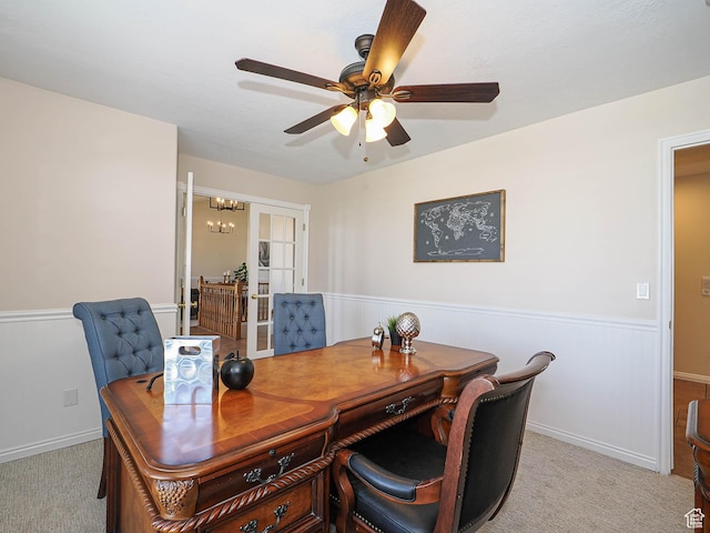 home office with ceiling fan with notable chandelier, light carpet, a wainscoted wall, and french doors