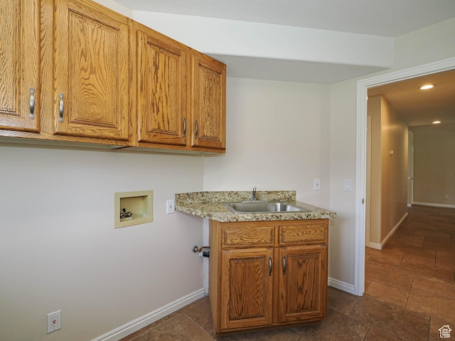 clothes washing area with stone tile floors, a sink, hookup for a washing machine, baseboards, and cabinet space