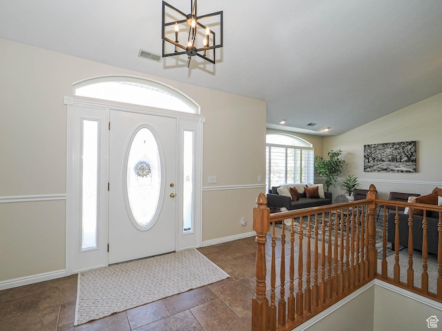 foyer featuring stone tile flooring, baseboards, visible vents, and a chandelier