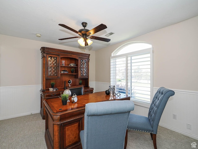 home office with wainscoting, visible vents, ceiling fan, and light colored carpet