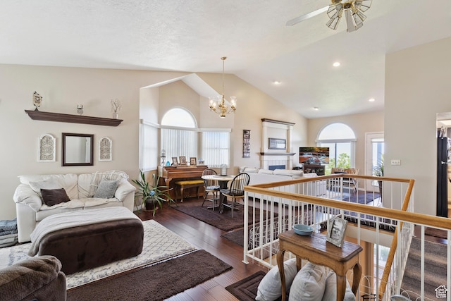 living room with ceiling fan with notable chandelier, a tiled fireplace, dark wood-style floors, vaulted ceiling, and recessed lighting