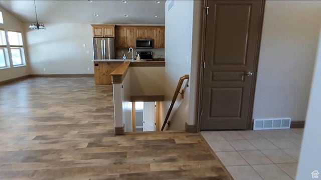 kitchen with appliances with stainless steel finishes, a sink, baseboards, light wood finished floors, and decorative light fixtures