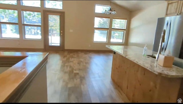 kitchen with light wood-type flooring, vaulted ceiling, baseboards, a chandelier, and light stone countertops