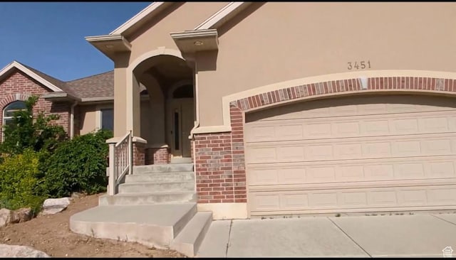 doorway to property with brick siding, stucco siding, and a garage